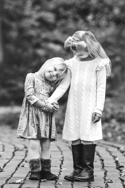 Little sisters stand hand in hand wearing dresses and boots.