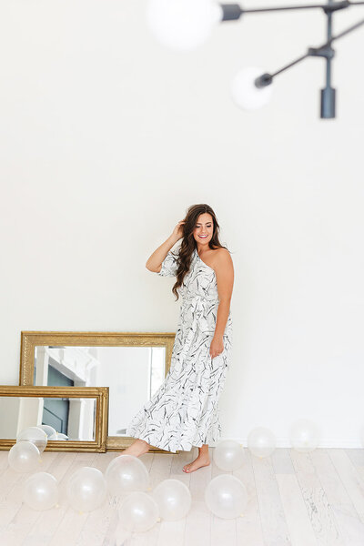 Abby Manawes in a long white and black dress kicking clear balloons on the floor