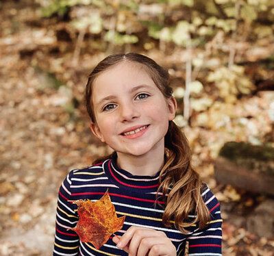 Caroline's daughter in the forest holding an orange leaf