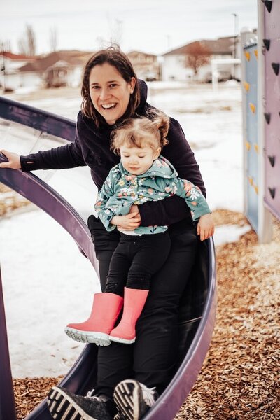 A mother holding her daughter in her lap slide down a slide together