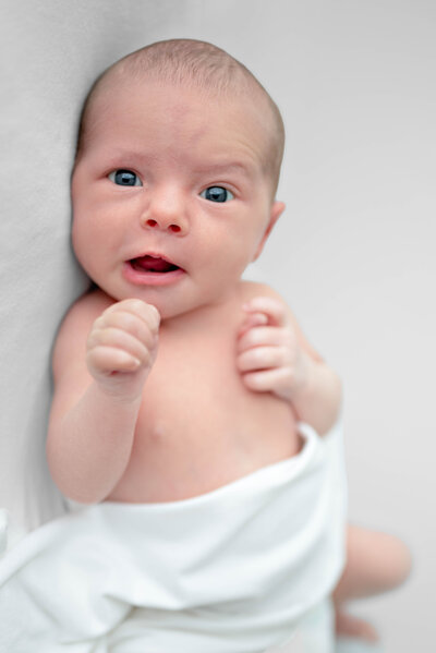 A newborn baby looks at the camera and smiles for his newborn pictures