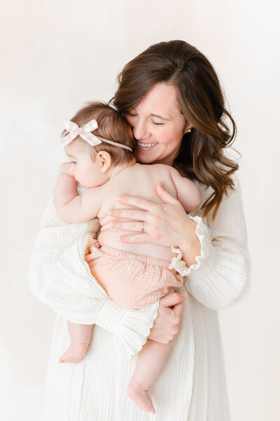 A dc family photography photo of a mother holding her daughter in pink bloomers in front of a hand-painted canvas backdrop