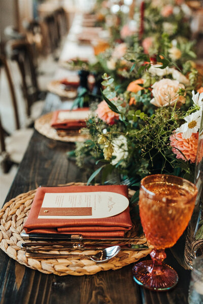Close up of a table with flowers and a wedding guest place setting with a customized calligraphy menu sitting on top of a cloth napkin. 
