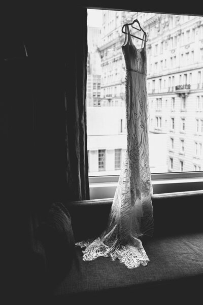 A wedding dress hangs in front of a window.