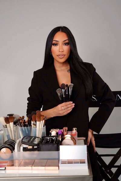 Best bridal makeup artist in NYC wearing an elegant black outfit, holding her luxury makeup products and tools used for on-location bridal services. Skinlux Beauty Bar, serving NYC, NJ & PA