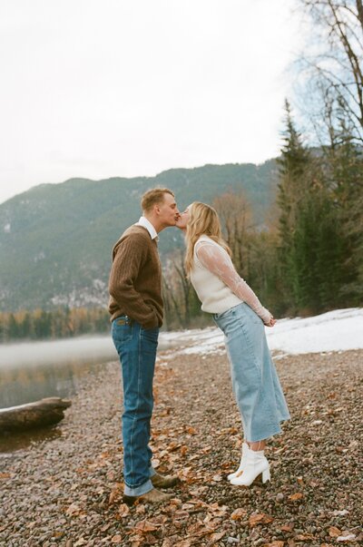 couple standing on shore of a lake in glacier kissing