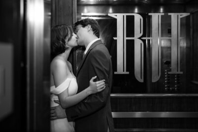 Black and white photo of the couple kissing in the vintage wood-paneled elevator of their Read House Wedding venue, with large “RH” initials reflected on the door.