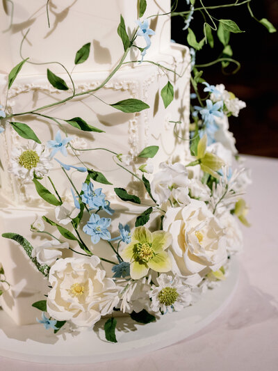 Detailed view of a multi-tiered wedding cake decorated with intricate white and blue flowers.
