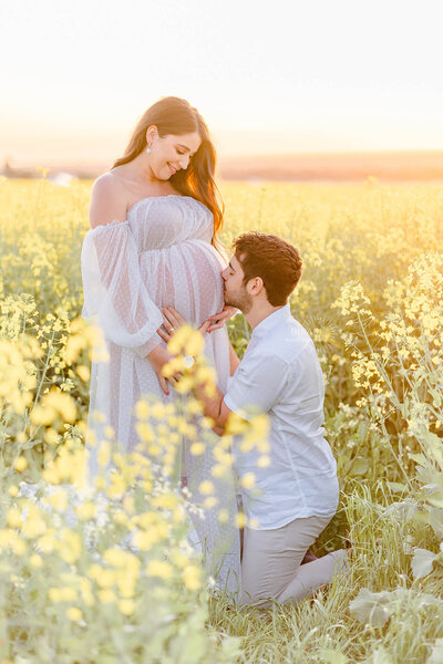 husband kneeling to kiss baby bump pregnant belly in isadora tulle dress in canola field gold coast