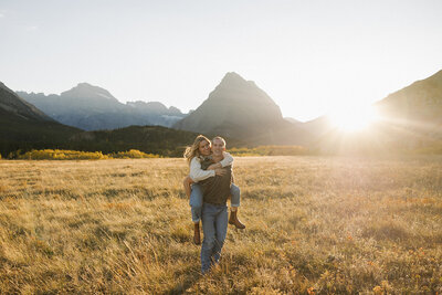 couple piggybacking through a field in Many Glacier at sunset