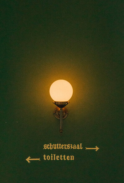 Warmly lit vintage wall sconce with elegant directional signage in Dutch, creating a timeless and moody atmosphere.