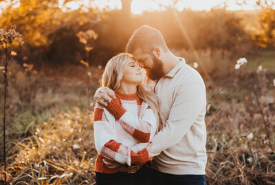 Engagement photoshoot with couple holding each other in field during golden hour