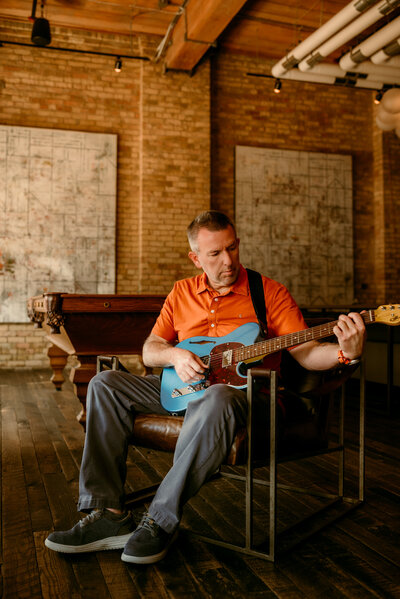 Professional dating portrait of Kerry in Minneapolis, smiling in an orange shirt while seated indoors, showcasing confidence and approachability.