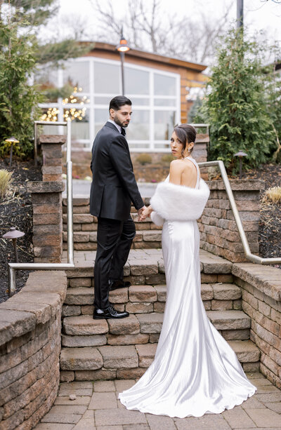 Groom escorts bride up stone stairs outside of Stonehouse Stirling Ridge in Warren, NJ