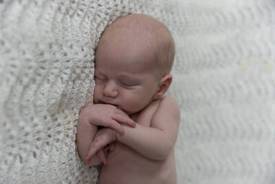 Nærbilde av nyfødt baby som ligger på et strikket hvitt teppe.