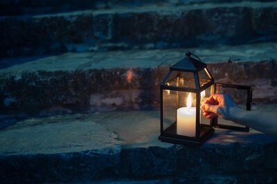 woman lighting a candle inside a lantern on brick steps