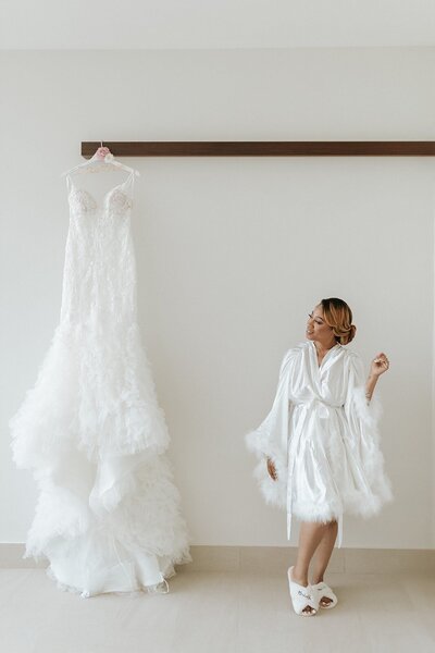Bride looks fondly at her wedding dress on a hanger.