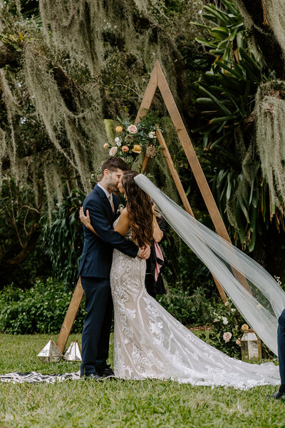 M&C Kissing under their wedding a frame arch.