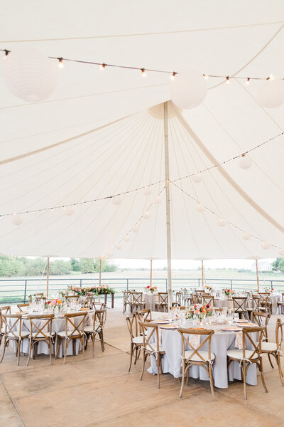 tented outdoor wedding reception with gray tablecloths and wooden chairs