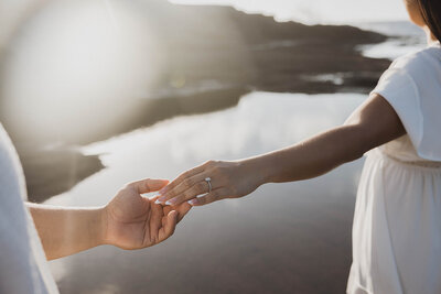 hands reaching for eachother in front of water with wedding ring