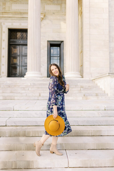 A woman wearing a floral dress and a hat on the steps of a building.