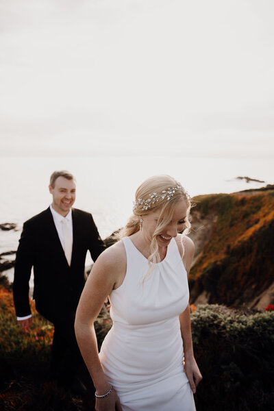 Bride and groom waling at cliffs of Carmel by the sea. Ocean and red soil in background