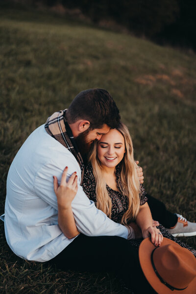 Engagement photo with couple holding each other sitting on a hillside during golden hour
