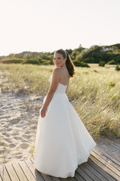 Meghan smiles while posing for photos in her wedding gown on the beach in Cape Cod Massachusetts. 