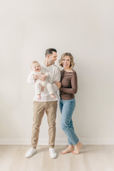 Mother, father, and one year old baby standing barefoot together inside a Kansas City studio during a first birthday cake smash session. 