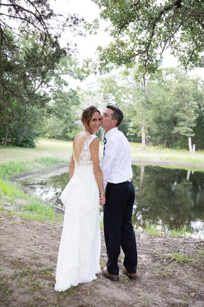 An Austin-based wedding photographer captures a beautiful moment as the bride and groom share a romantic kiss in front of a serene pond.