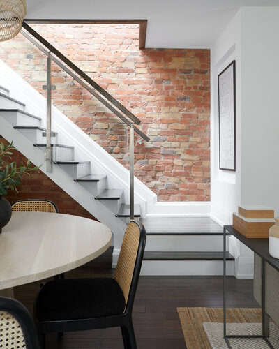 A black and white painted staircase next to a rough, red brick wall and in front of an elegant dining room area.