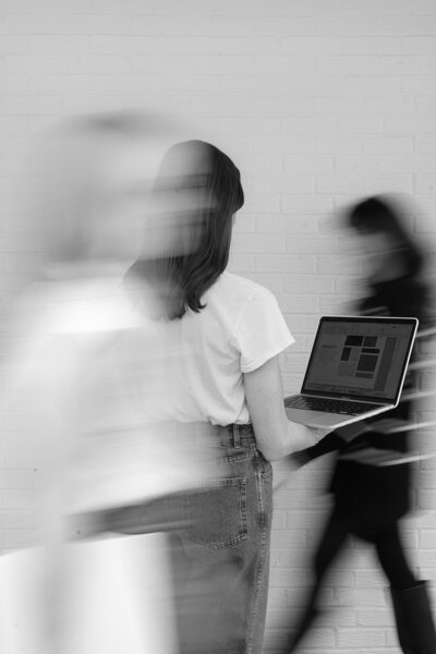 Black and white blurred photo of two women walking past a woman holding her laptop