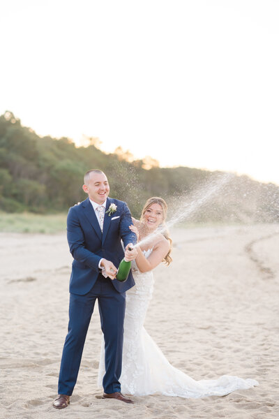 bride and groom popping champagne on the beach