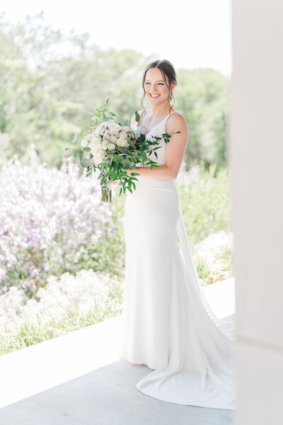 bride with white porcelain flower earrings, a cathedral length veil, holding a bouquet with eucalyptus and pink, white, and orange flowers