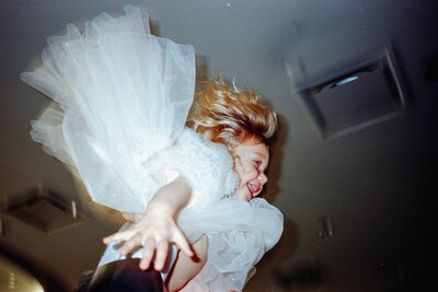 Little girl tossed in the air by her dad during a wedding reception in Potomac, Maryland — photographed on Portra 800 film with a point-and-shoot camera