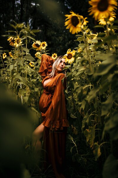 Pregnant woman in beautiful rust colored dress posing in a sunflower field