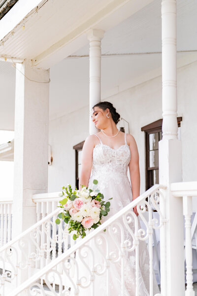 Bride holding a bouquet leaning against a pillar on a porch