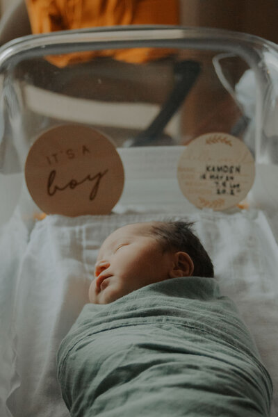 Newborn baby wrapped in a blanket with an "It's a Boy" sign