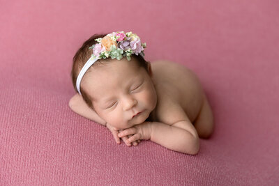 newborn girl sleeps on her belly for a portrait on a pink background