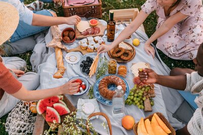 friends gather around a DIY simple picnic, with cake and berries and fruit, to share a special moment