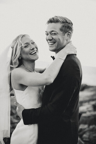 Bride and groom candidly laughing together while holding each other in black and white. 