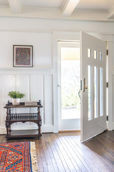 Entry with door open, white wainscot, hardwood floors, wood side table and vintage area rug