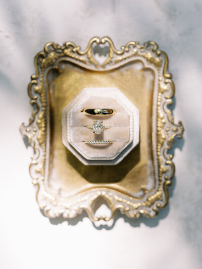 a diamond engagement ring and bride and groom wedding band on a gold tray