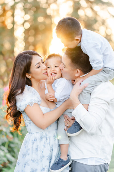 A family of four stand in a field of purple lupines dressed in shades of grey, blue, and white while smiling and holding one another photographed by bay area photographer, Light Livin Photography.