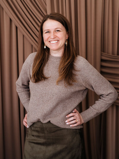 Kelly Planner/Lead Coordinator for Unique Melody Events & Design (New England Event Planners) standing  in front of orange wall decor