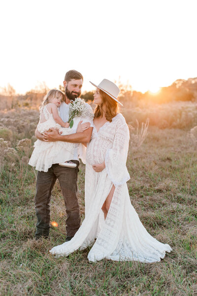 Boho styled Maternity session with mom in a beautiful hand made gown and wide brim hat. Daughter holding florals in dads arms at sunset