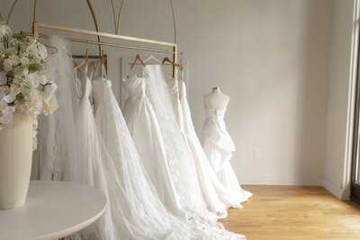 Rack of wedding dresses in a bridal shop with mannequin beside them.