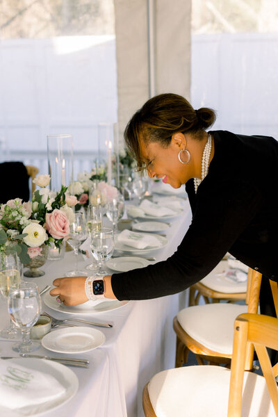 Woman setting up a table for a wedding reception with floral decor