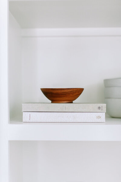 Two books and a wood bowl on a bookshelf.