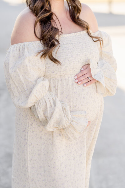 Close-up of a pregnant belly in a white dress with long sleeves.